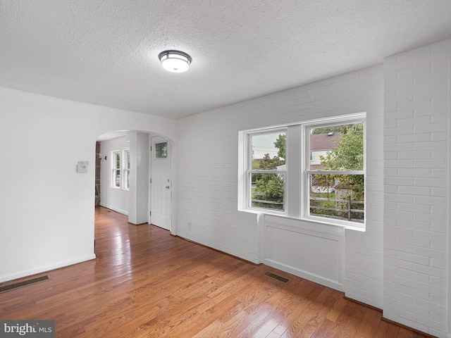 unfurnished room featuring wood-type flooring, a textured ceiling, and brick wall