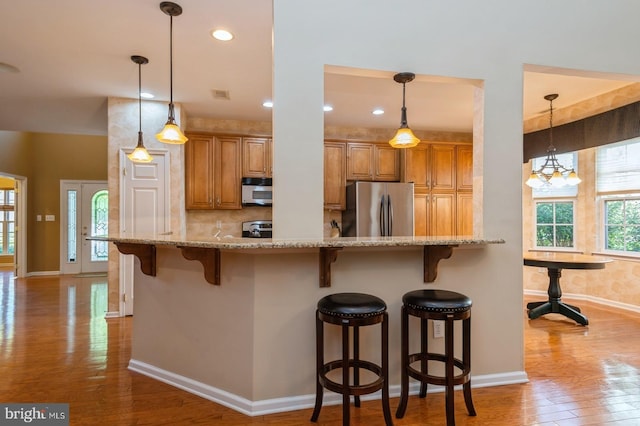 kitchen featuring light stone counters, a chandelier, stainless steel appliances, a breakfast bar area, and light hardwood / wood-style floors