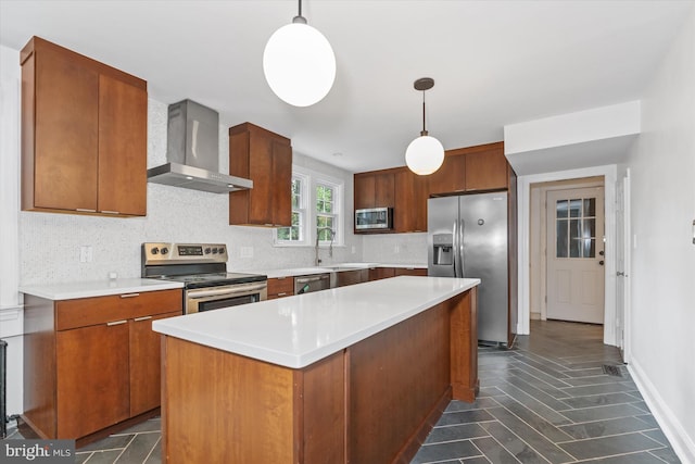 kitchen featuring a center island, appliances with stainless steel finishes, hanging light fixtures, and wall chimney range hood