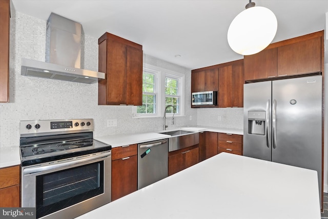 kitchen with sink, hanging light fixtures, wall chimney range hood, decorative backsplash, and stainless steel appliances