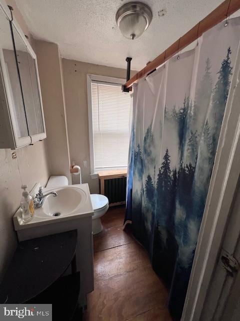 bathroom with a textured ceiling, radiator, hardwood / wood-style floors, vanity, and toilet