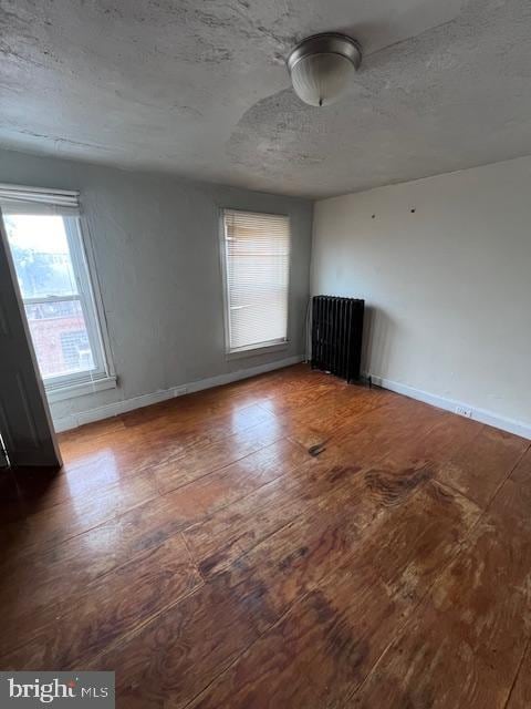 spare room with a textured ceiling, dark hardwood / wood-style flooring, and radiator heating unit