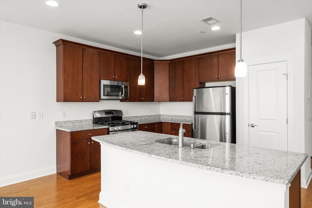 kitchen featuring light stone counters, stainless steel appliances, light wood-type flooring, decorative light fixtures, and sink