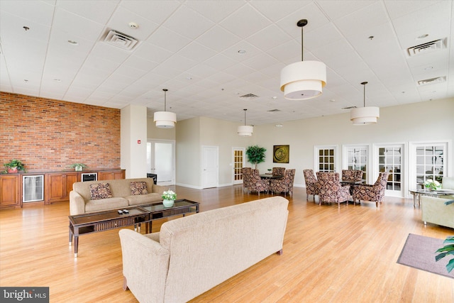 living room with a towering ceiling, wine cooler, light hardwood / wood-style floors, and brick wall