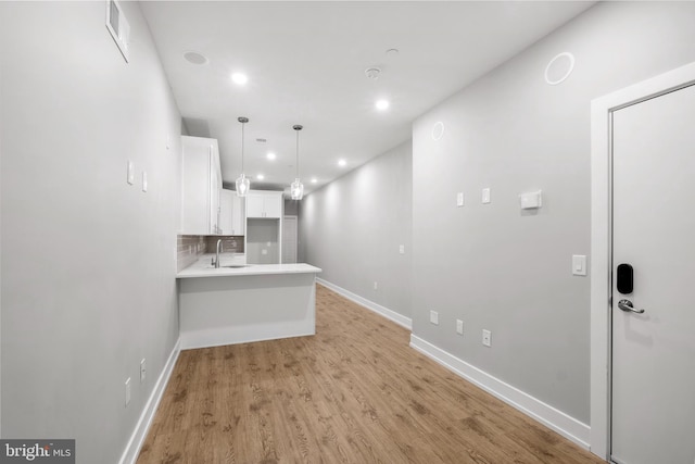 kitchen featuring decorative backsplash, sink, white cabinetry, light hardwood / wood-style flooring, and decorative light fixtures