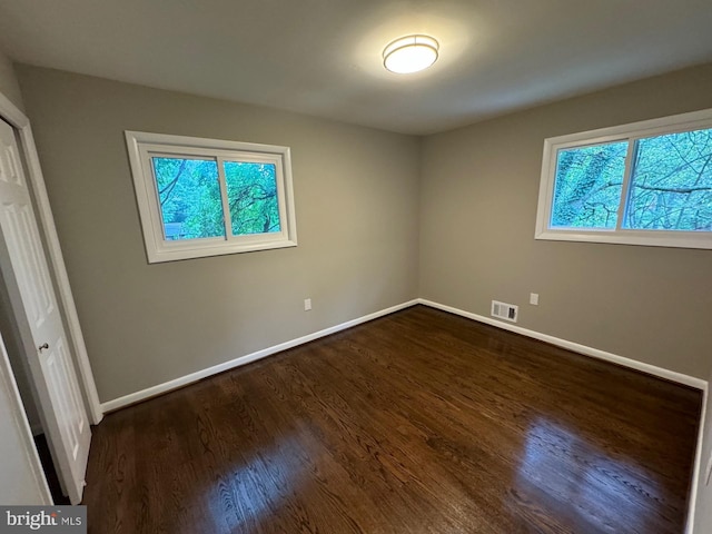 unfurnished bedroom featuring a closet, dark hardwood / wood-style floors, and multiple windows