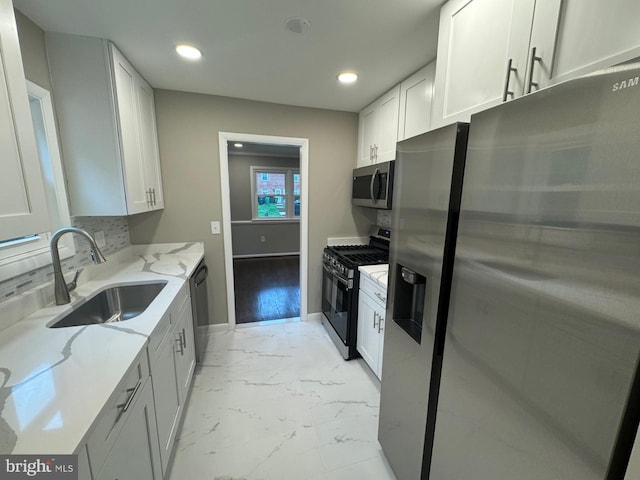 kitchen with appliances with stainless steel finishes, sink, light stone counters, and white cabinets