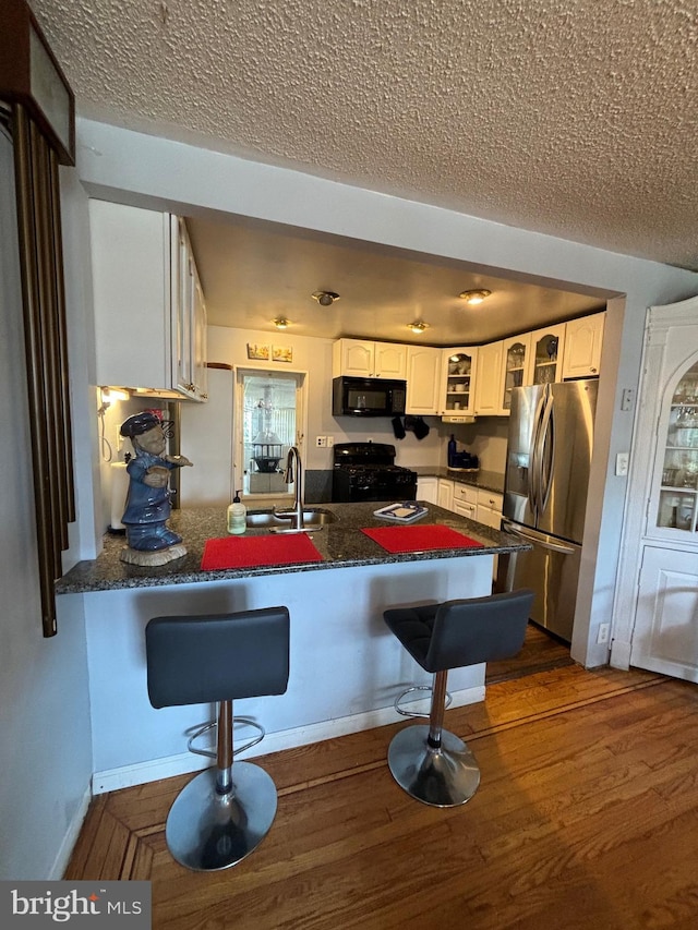 kitchen featuring white cabinets, a breakfast bar, kitchen peninsula, and black appliances