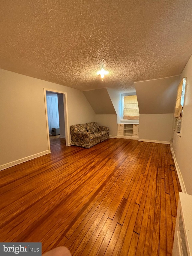 additional living space with a textured ceiling, vaulted ceiling, and hardwood / wood-style flooring