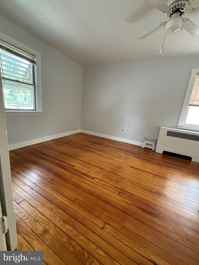 empty room with radiator heating unit, ceiling fan, a healthy amount of sunlight, and hardwood / wood-style floors