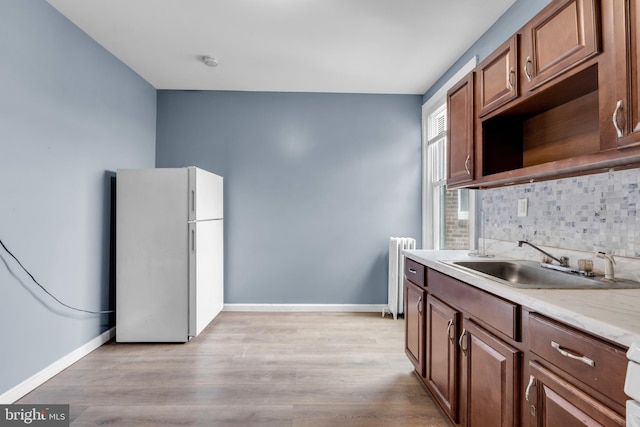 kitchen featuring light wood-type flooring, white refrigerator, tasteful backsplash, sink, and radiator