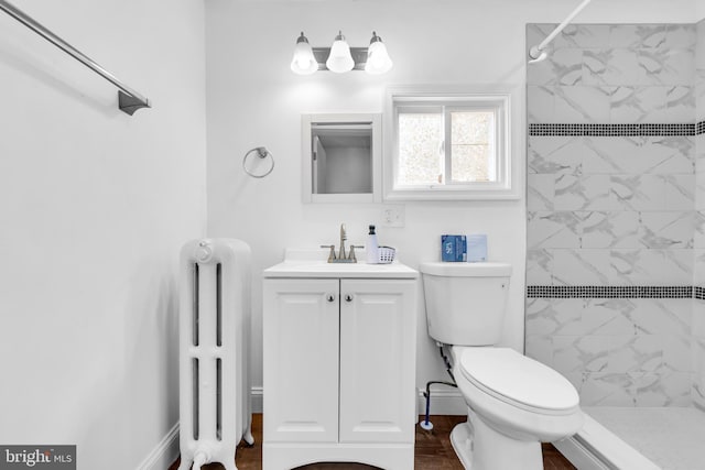 bathroom featuring radiator, vanity, toilet, a tile shower, and hardwood / wood-style floors