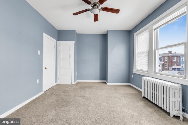 carpeted empty room featuring ceiling fan and radiator heating unit