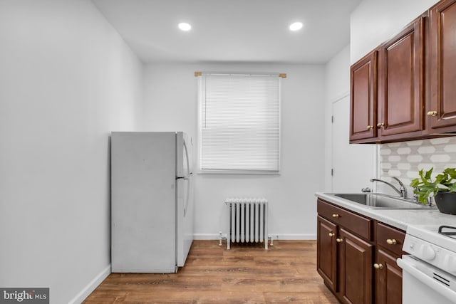 kitchen with radiator heating unit, white appliances, hardwood / wood-style floors, and sink