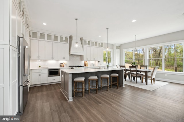 kitchen featuring a breakfast bar area, an island with sink, white cabinetry, decorative backsplash, and dark hardwood / wood-style flooring