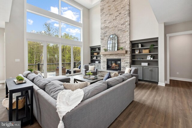 living room featuring a stone fireplace, a towering ceiling, dark hardwood / wood-style flooring, and built in features