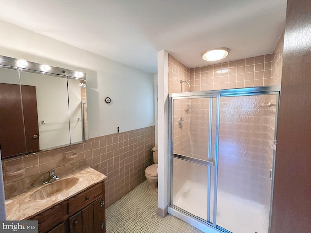 bathroom featuring toilet, vanity, tile walls, and a shower with door