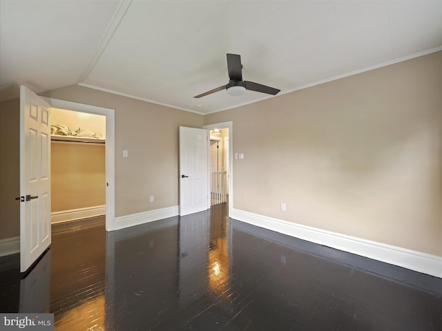 unfurnished bedroom featuring dark hardwood / wood-style flooring, a closet, ceiling fan, a walk in closet, and ornamental molding