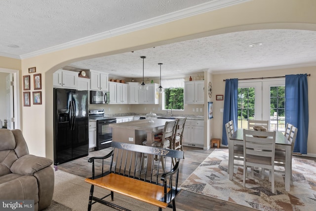 kitchen with hanging light fixtures, black appliances, a healthy amount of sunlight, and white cabinets