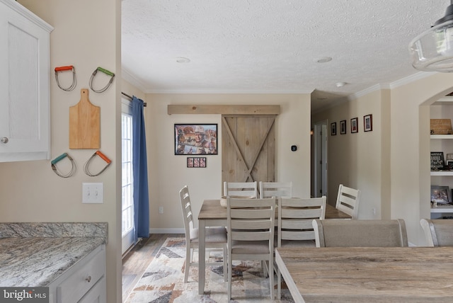 dining area featuring ornamental molding, light wood-type flooring, a healthy amount of sunlight, and a barn door