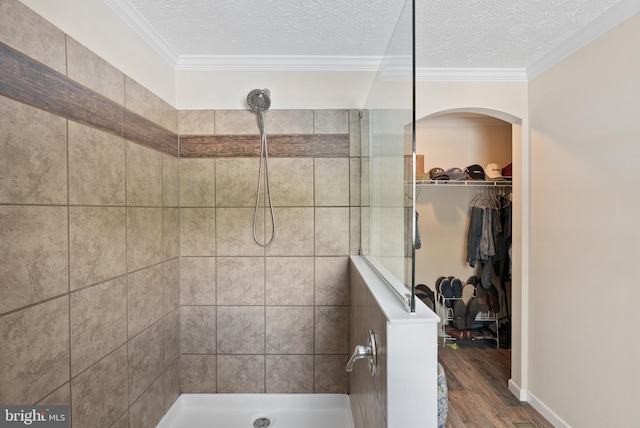 bathroom with wood-type flooring, ornamental molding, a textured ceiling, and a tile shower