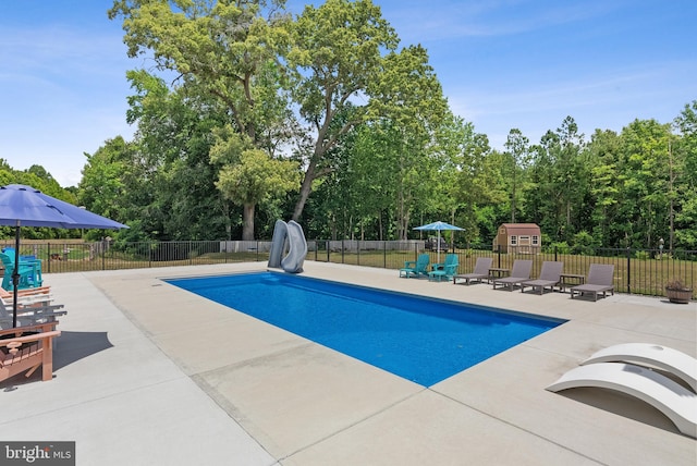 view of pool featuring a storage shed, a water slide, and a patio area