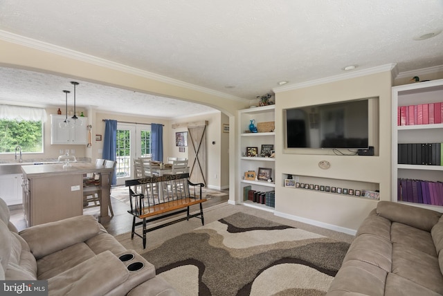 living room featuring a textured ceiling, french doors, built in shelves, ornamental molding, and sink