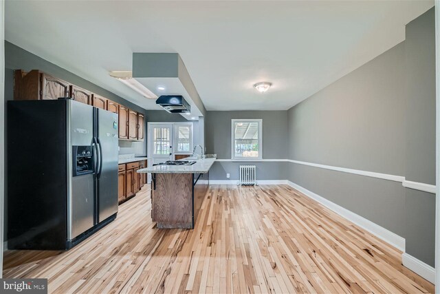 kitchen featuring radiator heating unit, a kitchen island, light hardwood / wood-style flooring, stainless steel refrigerator with ice dispenser, and a breakfast bar area