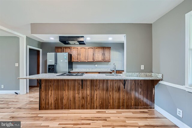 kitchen featuring light wood-type flooring, kitchen peninsula, sink, and stainless steel fridge