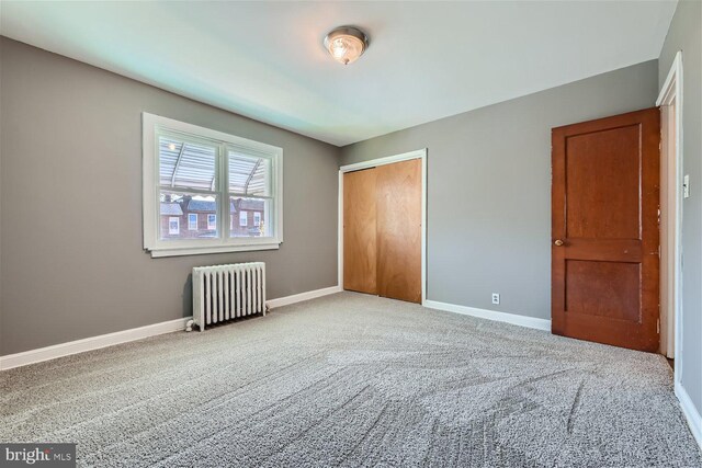 unfurnished bedroom featuring carpet flooring, radiator, and a closet