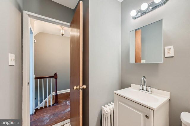 bathroom with wood-type flooring, radiator, vanity, and toilet