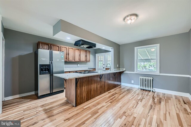 kitchen featuring light hardwood / wood-style floors, kitchen peninsula, radiator heating unit, stainless steel appliances, and sink