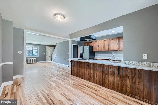 kitchen with kitchen peninsula, light wood-type flooring, radiator, stainless steel refrigerator with ice dispenser, and sink