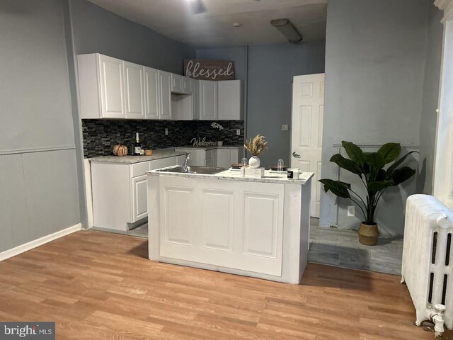 1128 Everett St, Camden, NJ 08104 - kitchen with light wood-style flooring, decorative backsplash, light countertops, radiator heating unit, and white cabinetry