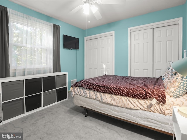 bedroom with two closets, carpet flooring, and ceiling fan