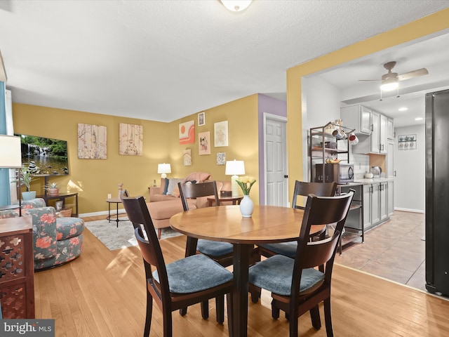 dining area with a textured ceiling, light wood-type flooring, and ceiling fan