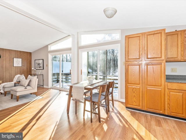 dining space with vaulted ceiling with beams, light wood-type flooring, and wood walls