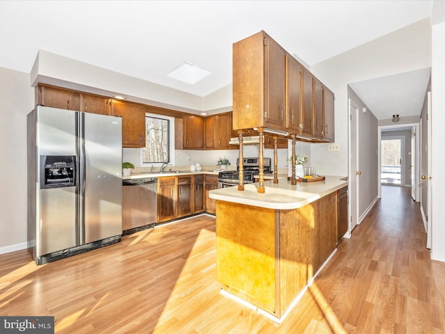 kitchen featuring sink, lofted ceiling with skylight, stainless steel appliances, kitchen peninsula, and light wood-type flooring