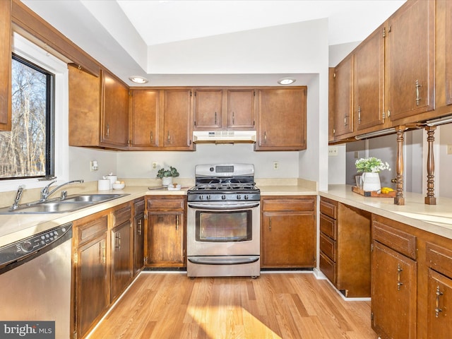 kitchen with vaulted ceiling, appliances with stainless steel finishes, sink, and light hardwood / wood-style flooring