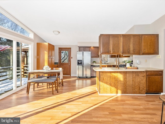 kitchen with light hardwood / wood-style floors, vaulted ceiling, stainless steel appliances, and kitchen peninsula