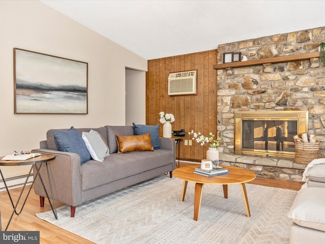 living room with vaulted ceiling, a stone fireplace, a wall mounted air conditioner, wood walls, and hardwood / wood-style flooring