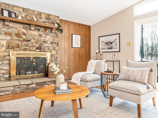 sitting room with a stone fireplace, light hardwood / wood-style floors, vaulted ceiling, and wood walls