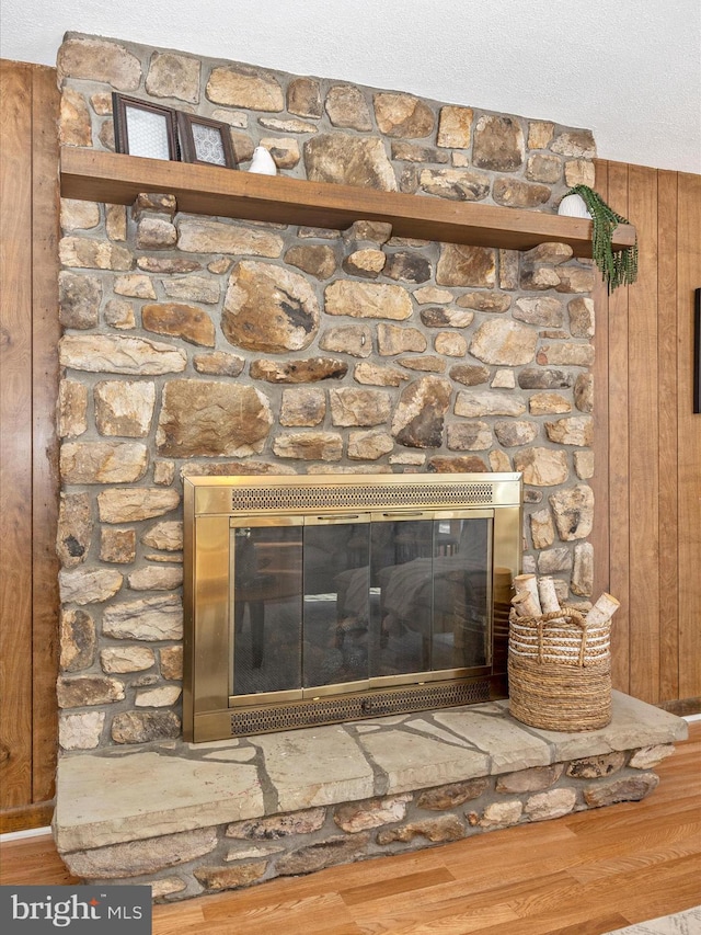 interior details with hardwood / wood-style flooring, a stone fireplace, wooden walls, and a textured ceiling