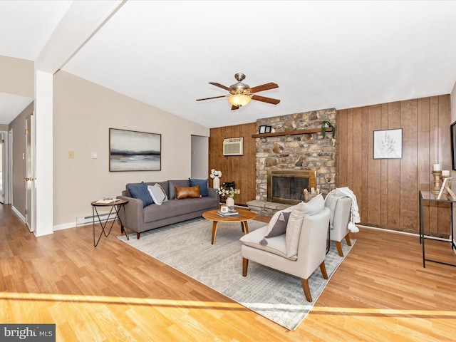 living room featuring lofted ceiling, wood-type flooring, wooden walls, and a stone fireplace