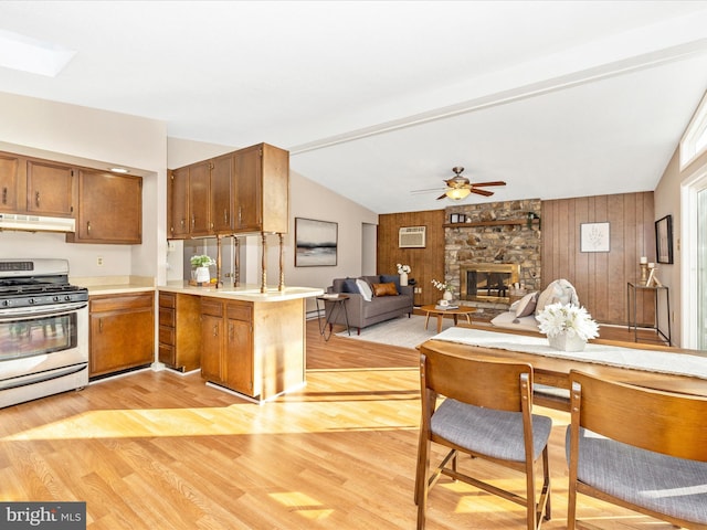 kitchen featuring light hardwood / wood-style flooring, stainless steel range with gas stovetop, a stone fireplace, kitchen peninsula, and wood walls