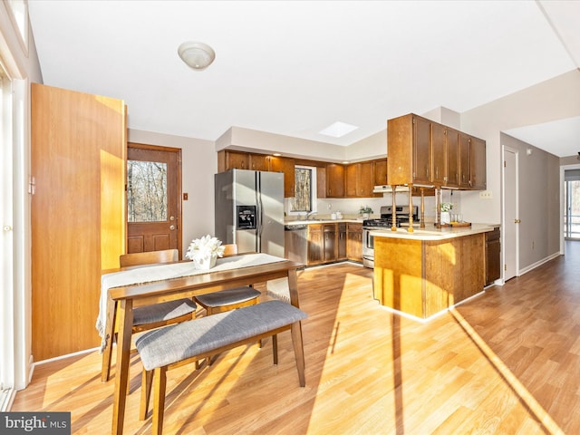 kitchen featuring appliances with stainless steel finishes, plenty of natural light, light wood-type flooring, and kitchen peninsula