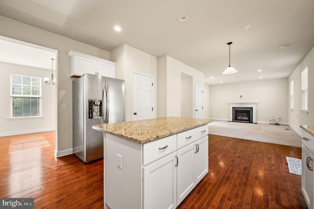 kitchen with light stone counters, white cabinets, stainless steel refrigerator with ice dispenser, hanging light fixtures, and a kitchen island