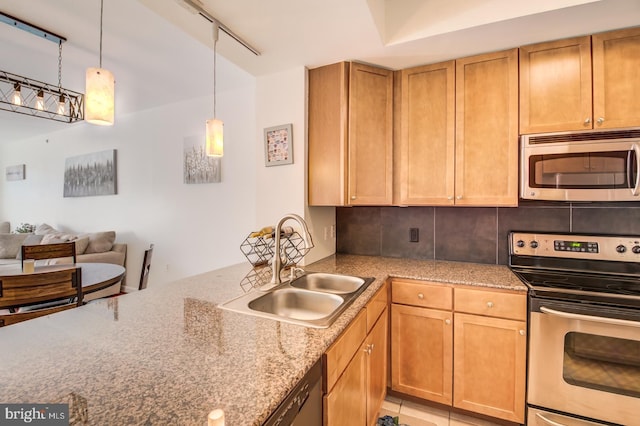 kitchen with track lighting, stainless steel appliances, sink, light stone countertops, and decorative light fixtures