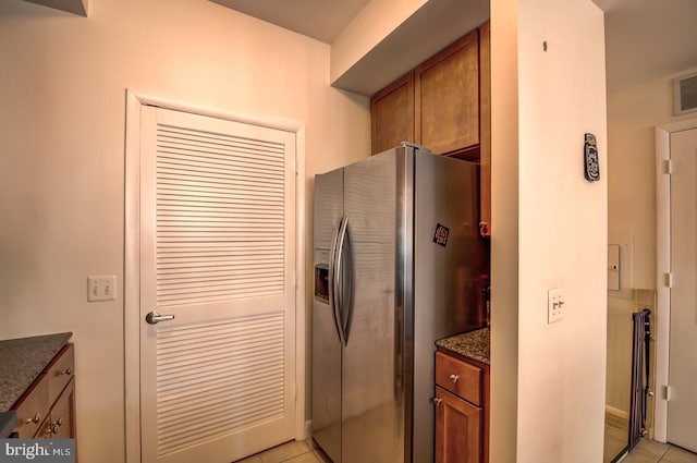 kitchen with stainless steel fridge, dark stone countertops, and light tile patterned flooring