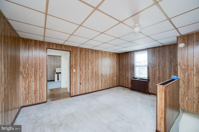 spare room featuring a paneled ceiling, wooden walls, and radiator heating unit